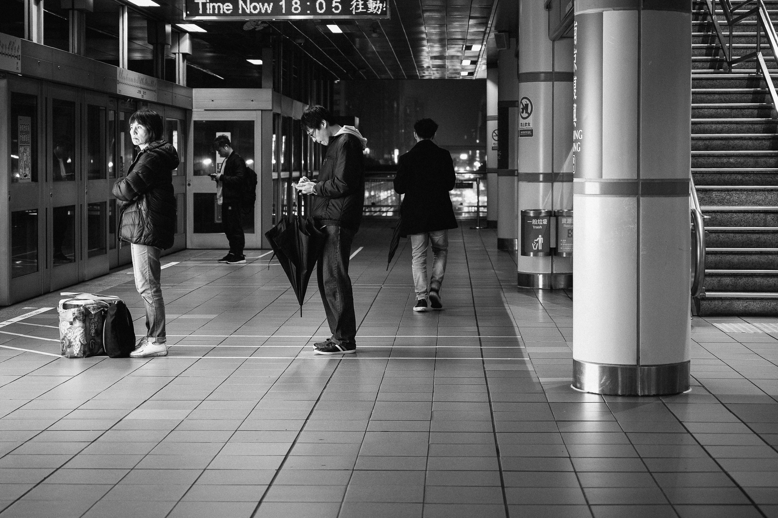 Four travellers waiting separately beneath a station clock