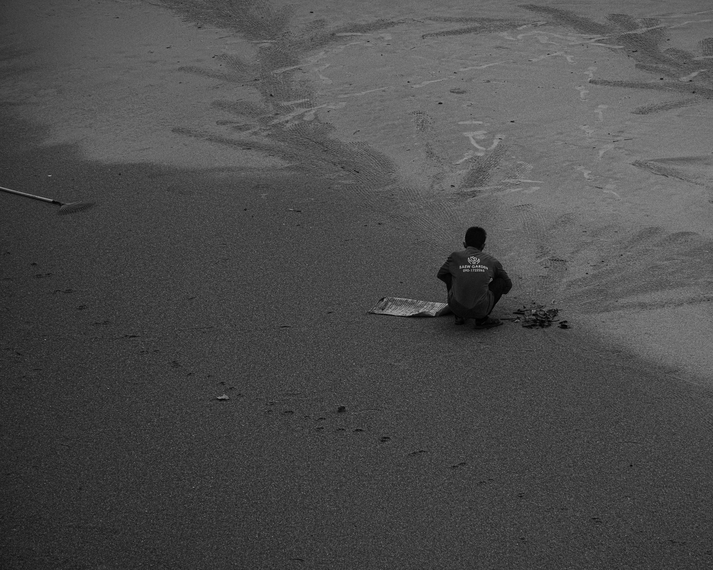 A beach worker resting alone beside his rake