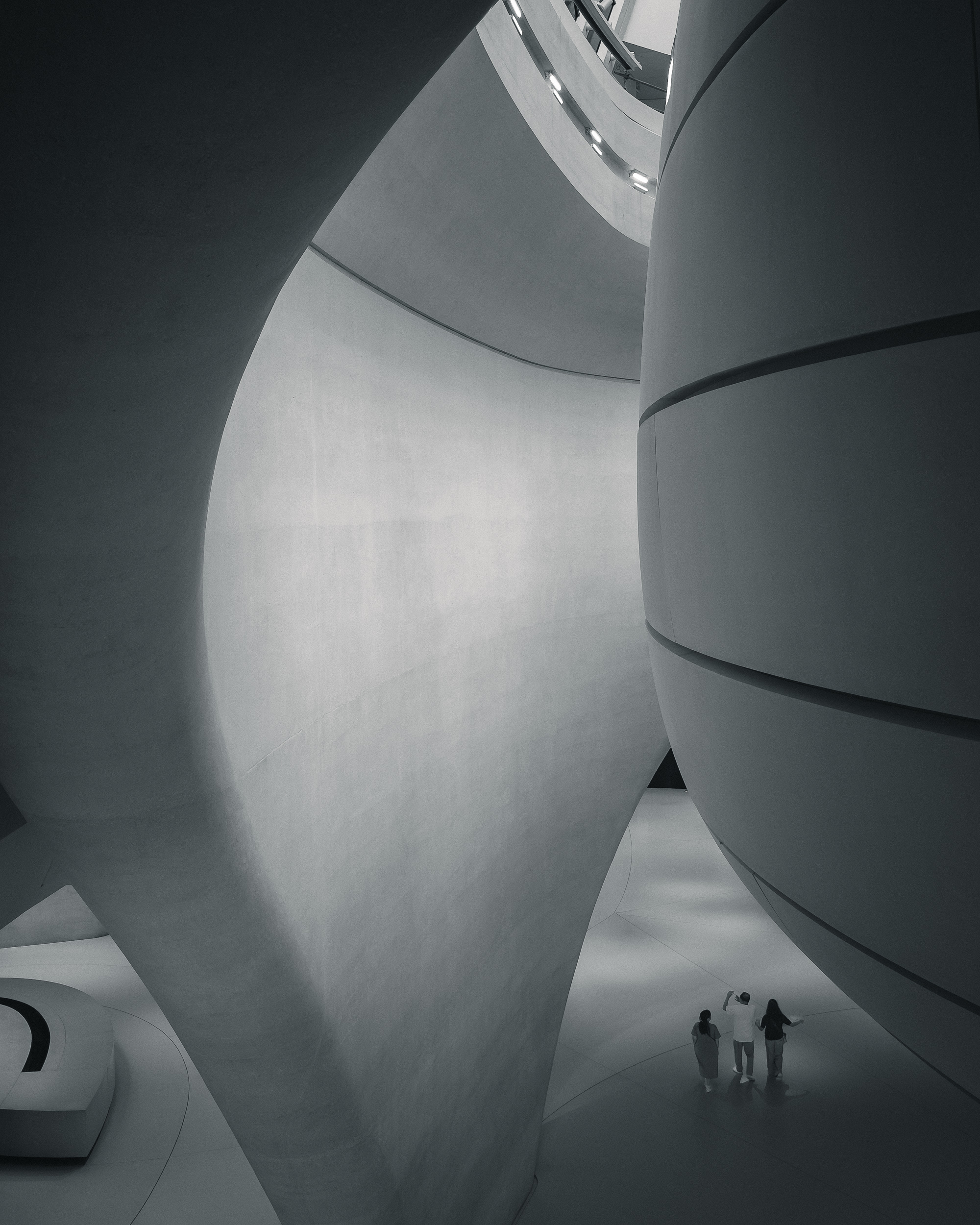 Three visitors dwarfed by the monumental curves of a museum interior